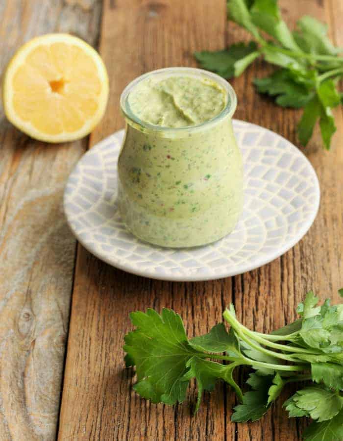 Green goddess dressing in a container on a plate with parsley and a lemon wedge