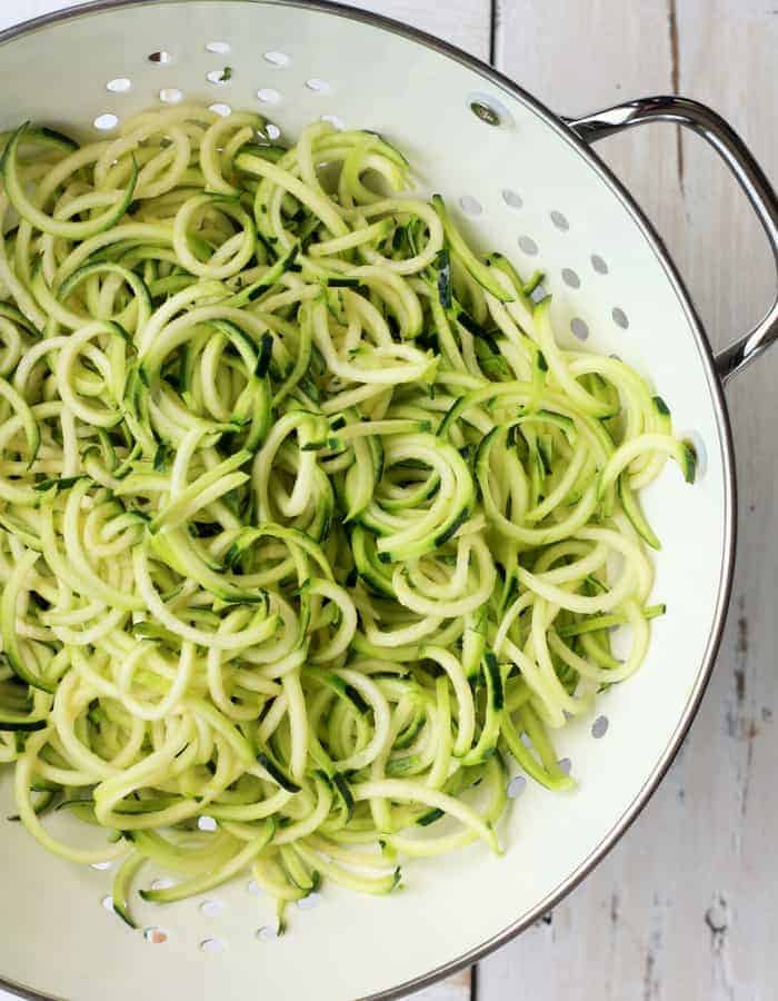 a white colander with zucchini noodles