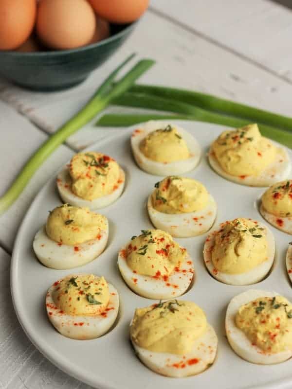deviled eggs with greek yogurt on a tray with green onions and a bowl of eggs in the background