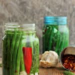 Two jars of dilly beans with garlic and red peppers on a wooden board