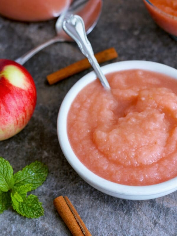 A bowl of bowl of homemade applesauce with cinnamon sticks and apples on a grey board