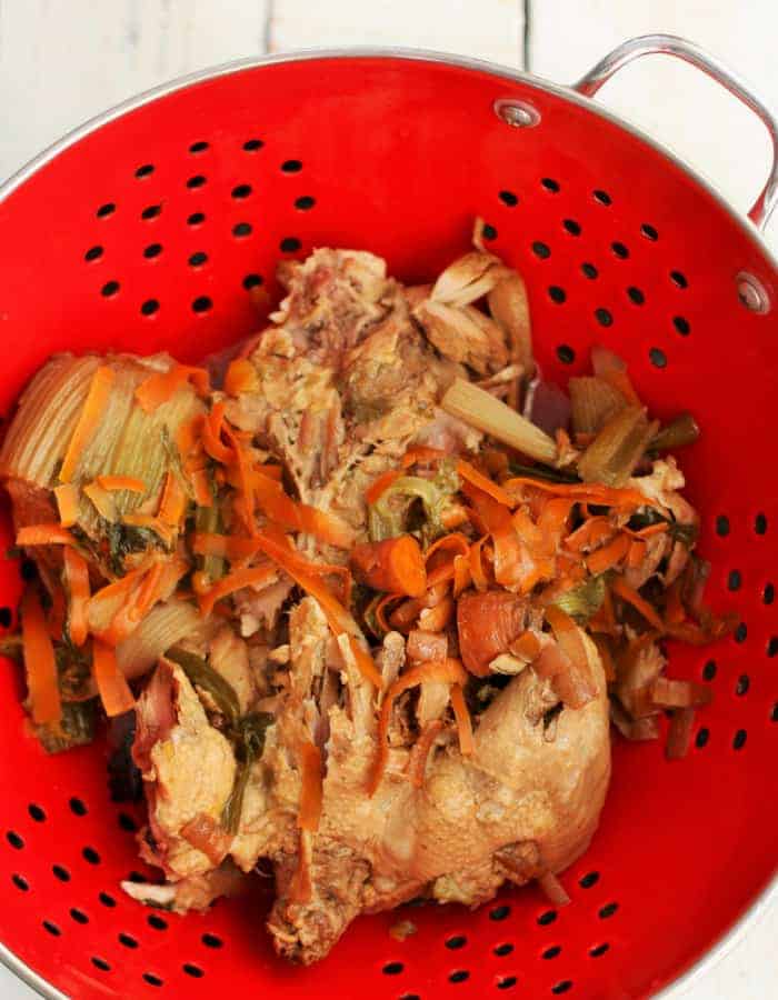 cooked chicken and vegetable scraps in a red strainer