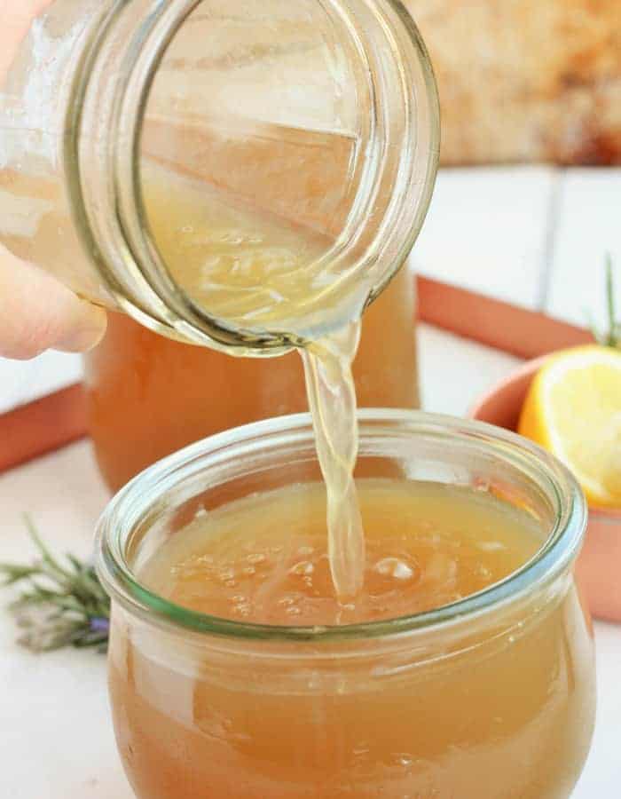 homemade chicken stock being poured into a small glass jar