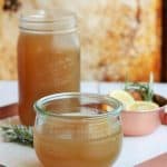 homemade chicken stock in jars on a white tray with rosemary and lemon