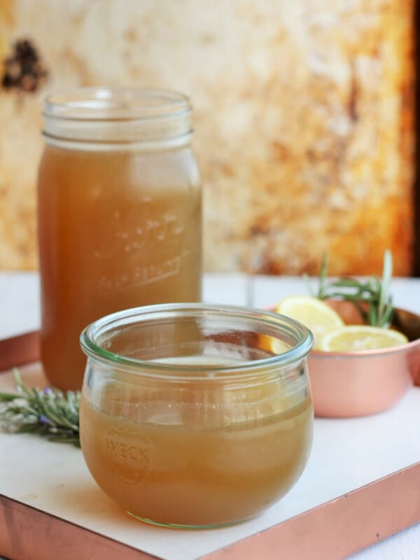 homemade chicken stock in jars on a white tray with rosemary and lemon