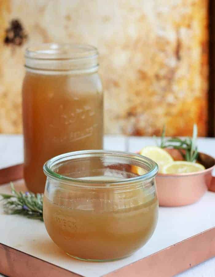 homemade chicken stock in jars on a white tray with rosemary and lemon