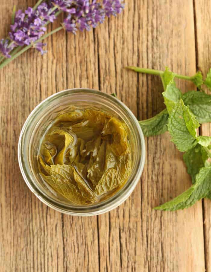 A jar of peppermint extract with mint and lavender on a board