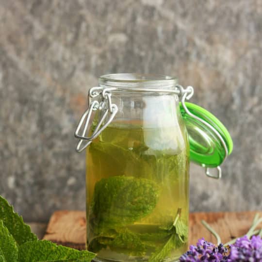A bottle of homemade peppermint extract with mint and lavender on a wooden board