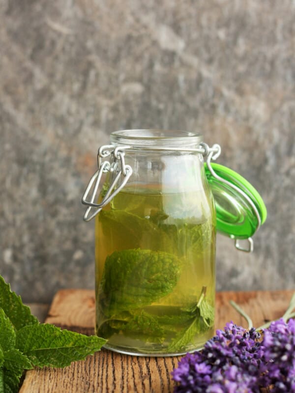 A bottle of homemade peppermint extract with mint and lavender on a wooden board