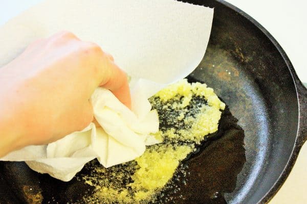 a hand using a paper towel to scrub salt into a cast iron skillet to remove rust