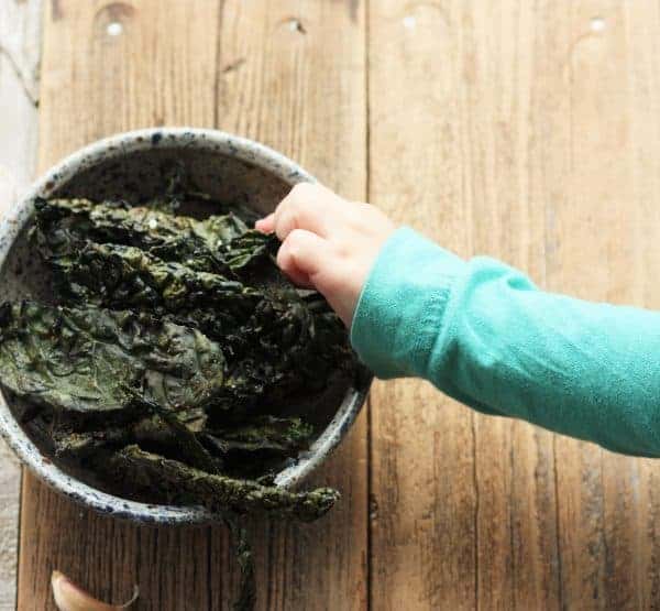 a toddler's hand reaching for a bowl of kale chips