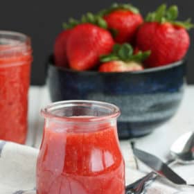 Strawberry jam in a small jar with a bowl of strawberries in the background