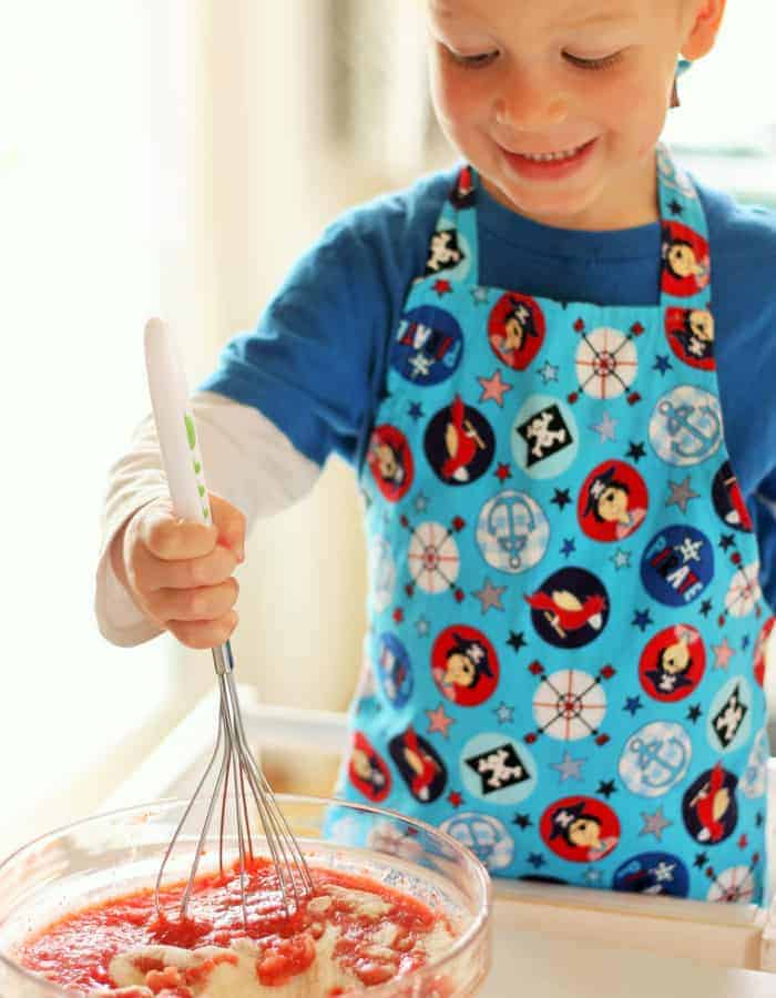 a little boy in an apron making strawberry freezer jam