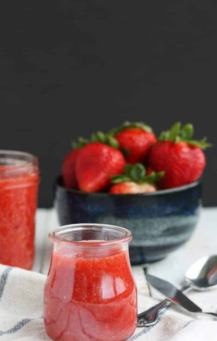 a jar of strawberry freezer jam with a bowl of fresh strawberries