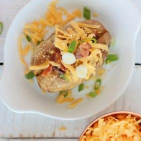 baked potato on a white dish with cheese, bacon, and green onions