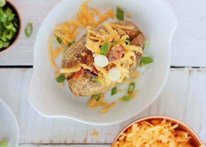 baked potato on a white dish with cheese, bacon, and green onions