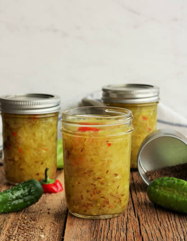 Three jars of homemade dill relish with cucumbers and a pepper