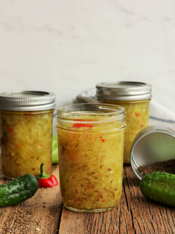 Three jars of homemade dill relish with cucumbers and a pepper