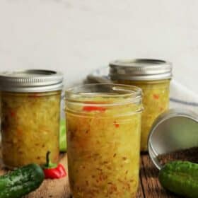 Three jars of homemade dill relish with cucumbers and a pepper