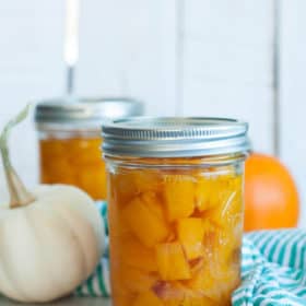 Jars of canned pumpkin with two mini pumpkins and a green striped cloth