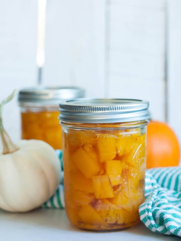 Jars of canned pumpkin with two mini pumpkins and a green striped cloth