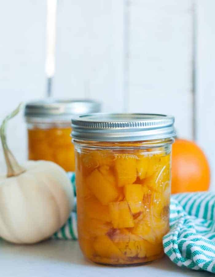 Jars of canned pumpkin with two mini pumpkins and a green striped cloth