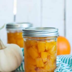 Jars of canned pumpkin with two mini pumpkins and a green striped cloth