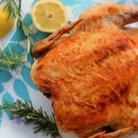 Roasted chicken on a white platter with rosemary and fresh lemons