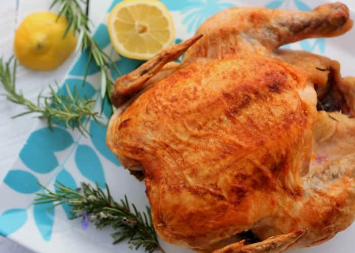 Roasted chicken on a white platter with rosemary and fresh lemons