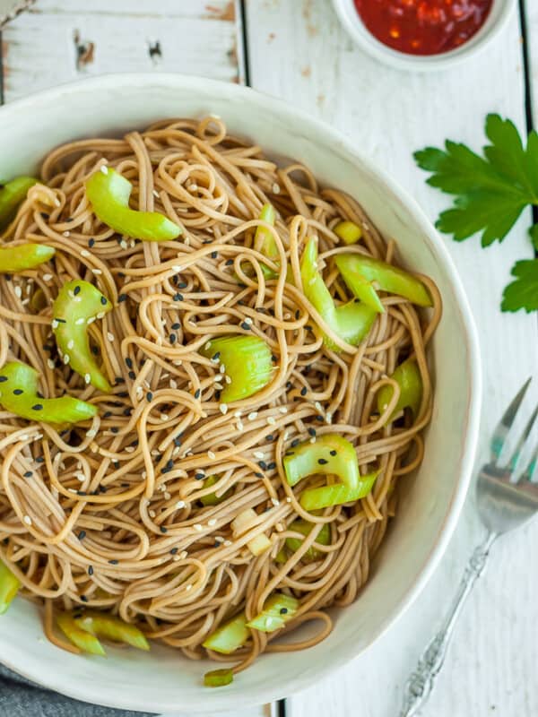 A white bowl filled with soba noodles topped with green onions and celery