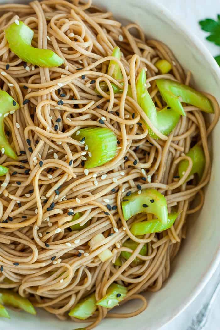 A close up shot of a bowl of cold noodle salad topped with sliced celery and green onions