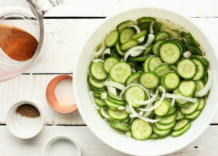 A white bowl full of cucumber and onion slices, and small bowls full of salt and dill
