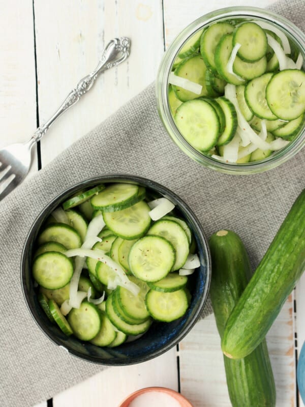 cucumber and onion salad in two bowls with persian cucumbers and a fork on a white background
