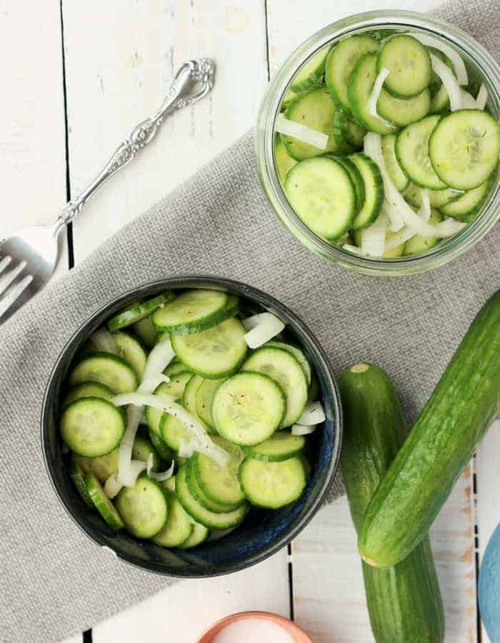 cucumber and onion salad in two bowls with cucumbers and a fork on a white background
