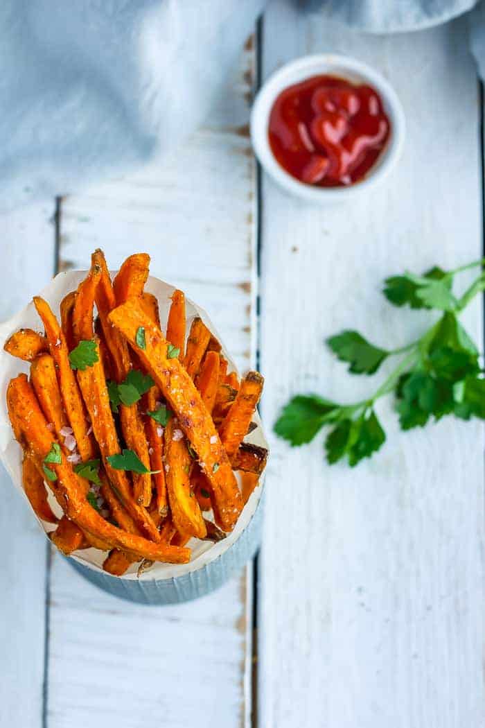A container of spicy sweet potato fries with parsley and ketchup