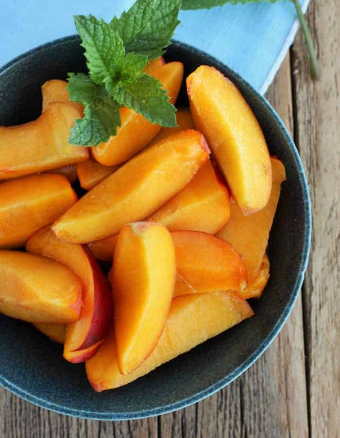 Sliced peaches in a dark green bowl with mint