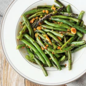 a round white plate full of green bean stir fry