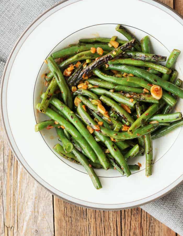 a round white plate full of green bean stir fry