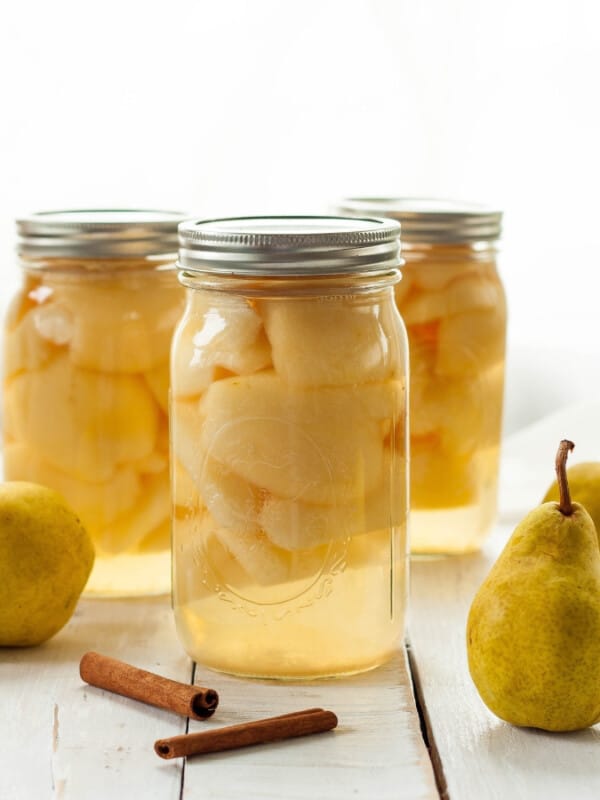 Three jars of canned pears on a wooden board with fresh pears and cinnamon sticks