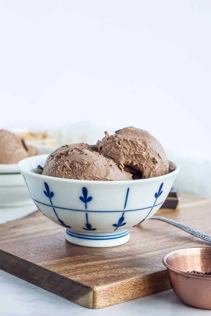 dairy-free chocolate ice cream in a white bowl with blue decorations and a spoon on a wooden board