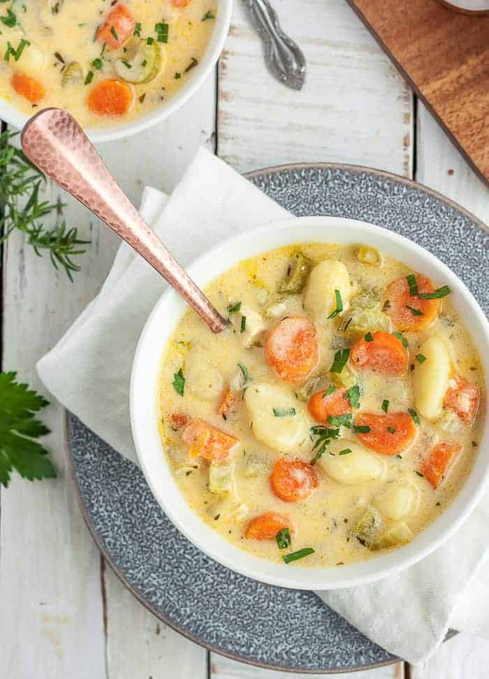 a bowl of chicken gnocchi soup on a grey plate with a white napkin