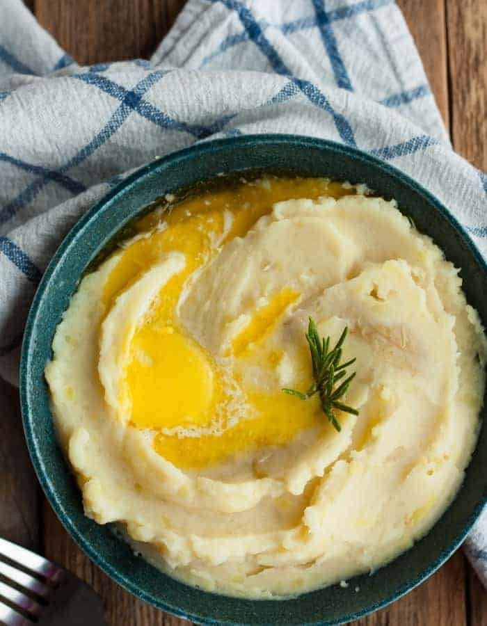 fluffy mashed potatoes in a bowl topped with butter and rosemary
