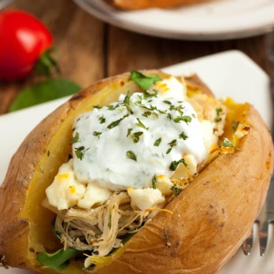 An chicken stuffed instant pot sweet potato on a plate with tomatoes and herbs