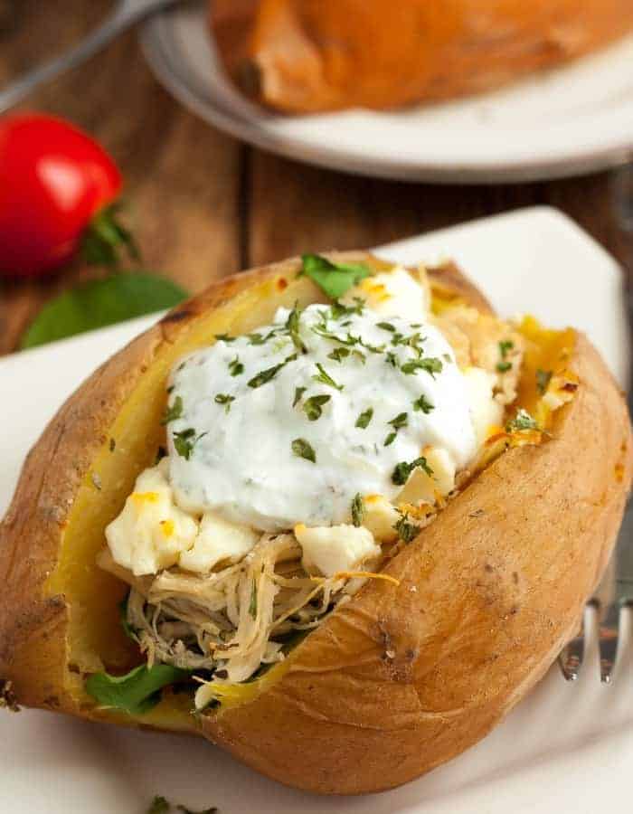 An chicken stuffed instant pot sweet potato on a plate with tomatoes and herbs