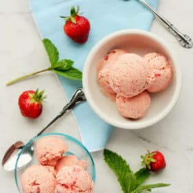 two bowls of homemade strawberry ice cream with mint and whole strawberries
