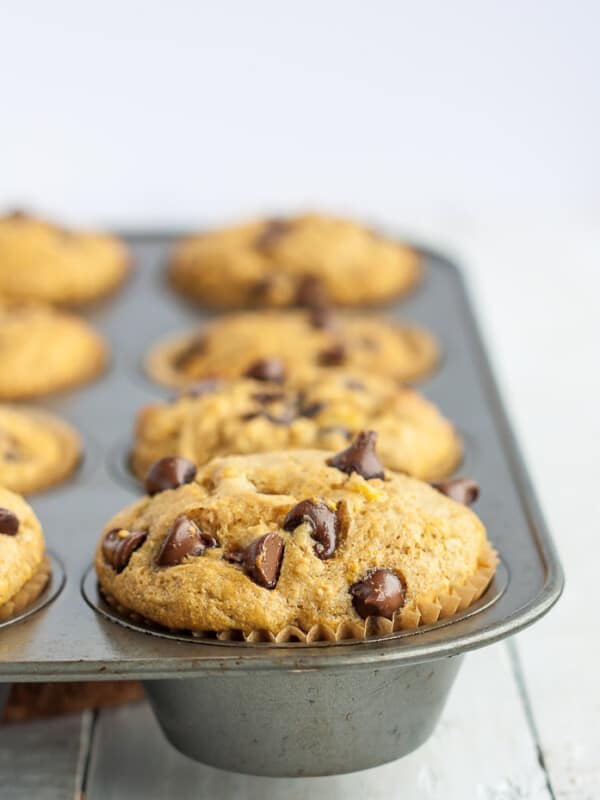 a muffin tray with a fluffy healthy banana chocolate chip muffin in focus