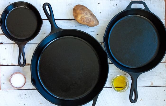 a potato, salt, and olive oil with three cast iron skillets that have been seasoned