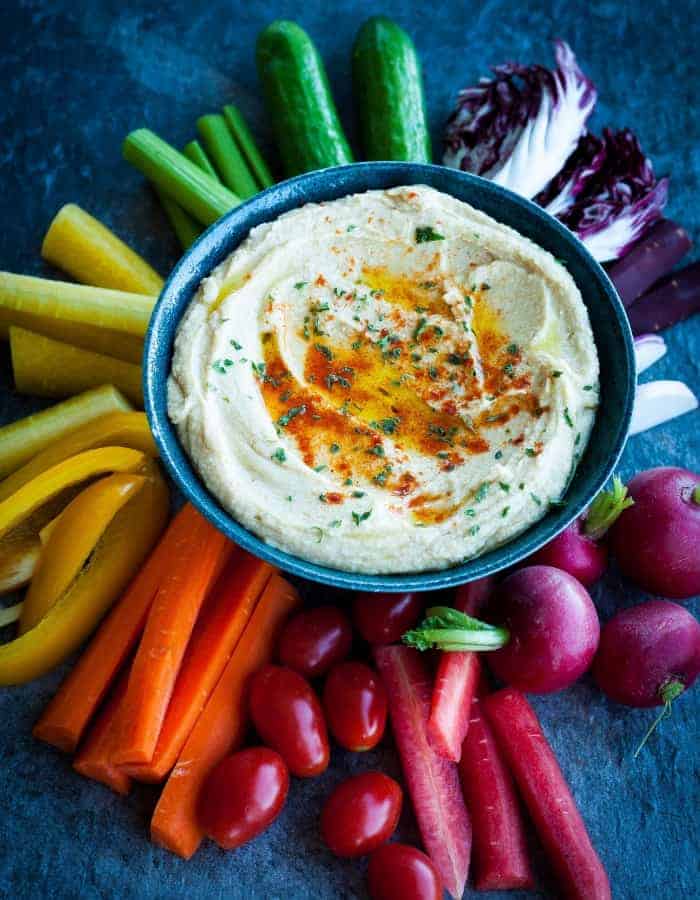 garlic hummus recipe in a bowl surrounded by colorful vegetables