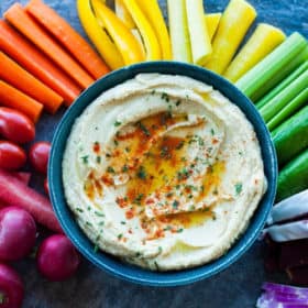 a rainbow of veggies with a bowl of garlic hummus recipe in the middle