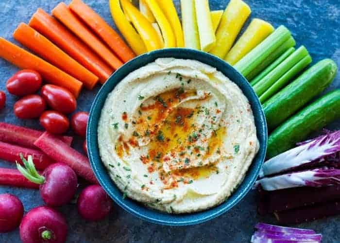 a rainbow of veggies with a bowl of garlic hummus recipe in the middle